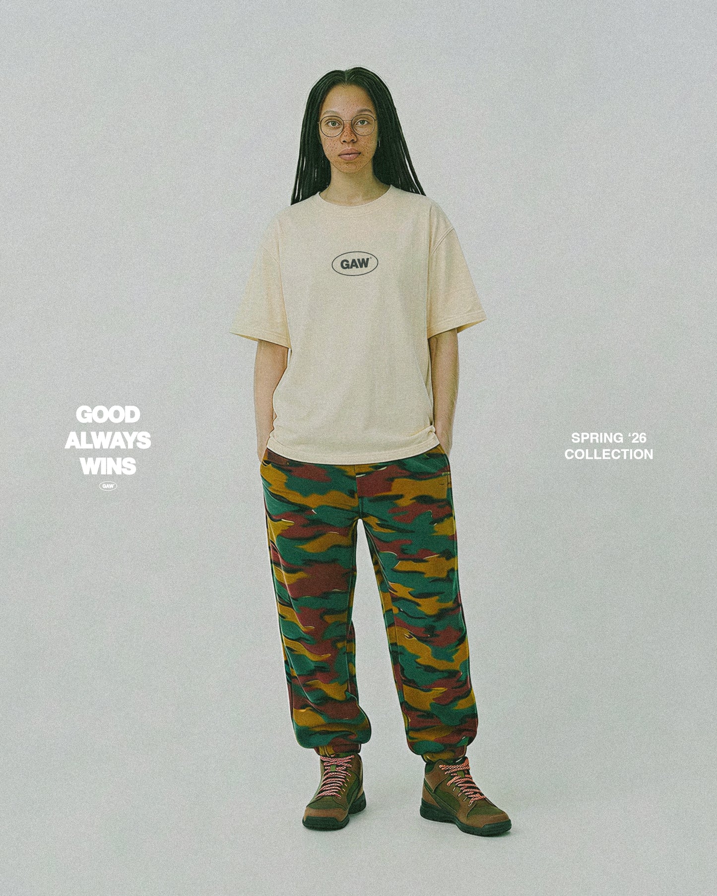 Person wearing a beige t-shirt and colorful camouflage pants on a white background with text. Good Always Wins